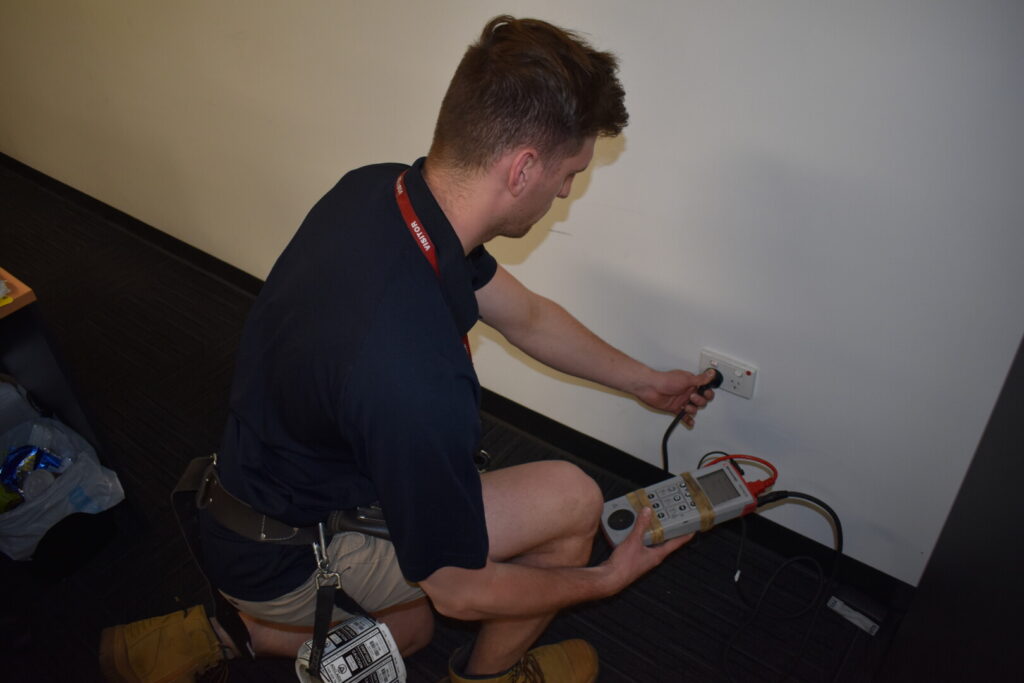 Technician performing RCD safety switch testing with a testing device, ensuring electrical safety compliance in a commercial setting.