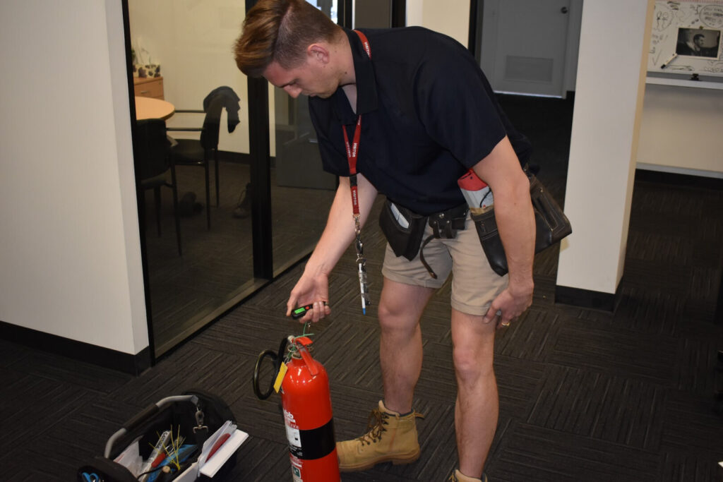 Technician inspecting fire extinguisher during professional testing service in office environment, ensuring compliance with fire safety standards.
